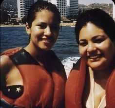 two women in life vests on a boat near the water with buildings in the background