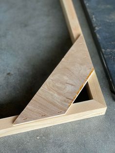 an unfinished piece of wood sitting on top of a cement floor next to a hammer