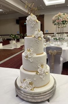 a three tiered wedding cake with white and gold flowers on the top is sitting on a table