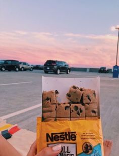 someone holding up a bag of cookies in front of some parked cars on the street