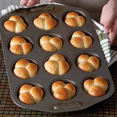 a person holding a muffin tin with heart shaped rolls in it