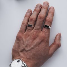 a person's hand with two rings on it and a watch in the background