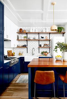 a kitchen with blue cabinets and wooden counter tops, two chairs are facing the island