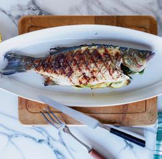 a grilled fish on a white plate next to a knife and fork