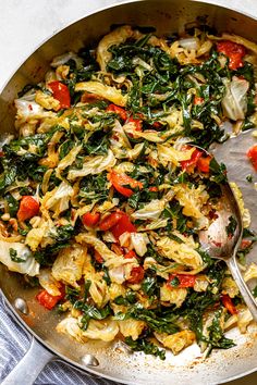 a skillet filled with pasta and vegetables on top of a blue towel next to a silver spoon