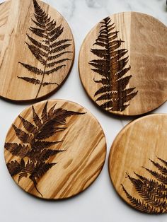 four wooden coasters with different types of leaves on them, one is brown and the other is green