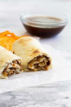 two burritos cut in half sitting on top of white paper next to an orange slice