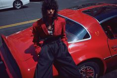 a woman leaning on the hood of a red car