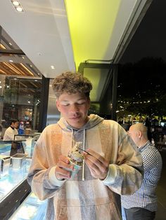 a young man standing in front of a display case looking at his cell phone and eating something