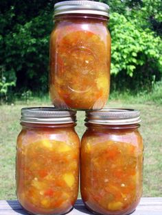 four jars filled with food sitting on top of a wooden table in front of trees