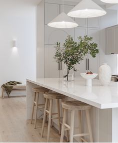 a kitchen with white counter tops and stools next to a plant in a vase