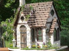 a miniature house made out of stone with flowers growing on the roof and window sill