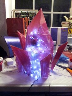 an origami sculpture with blue lights on it's head sits on a table in front of a window