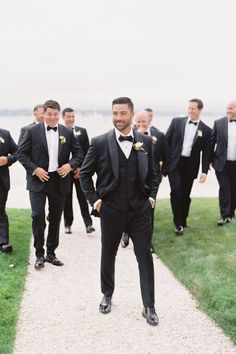 a group of men in tuxedos walking down a path next to the ocean