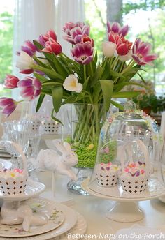 a table topped with plates and vases filled with pink tulips on top of a white table cloth