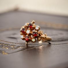 This stunning 9ct gold dress ring showcases four vibrant garnets, beautifully complemented by five sparkling dainty opals. The ring's design is inspired by the Victorian period, featuring intricate scrollwork to the shoulders for a touch of antique elegance. Garnets have long been cherished for their believed protective powers, thought to safeguard travellers and illuminate the night, symbolising guidance and safety. This rich symbolism has made garnets a timeless favourite in jewellery for both Garnet Dress, Giacomo Casanova, Victorian Period, Dress Ring, Dress Rings, Vintage Ring, Gold Dress, Rings Statement, Vintage Rings