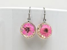 pink dandelion earrings with gold flecks on them are sitting on a white surface