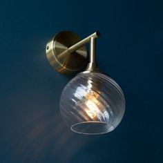 a wall light that is on the side of a blue wall and has a clear glass ball hanging from it