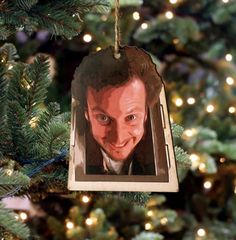 a christmas ornament hanging from a tree with lights in the background and an image of a man's face on it