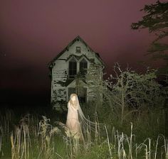 a ghostly ghost standing in front of an old house at night with the lights on