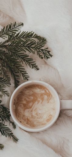 a cup of coffee sitting on top of a white blanket next to a pine tree