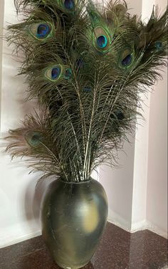 a vase filled with lots of peacock feathers on top of a table next to a wall