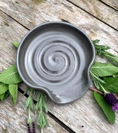 a metal bowl sitting on top of a wooden table next to green leaves and purple flowers