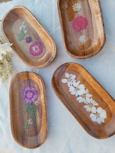 four wooden trays with flowers painted on them sitting on a white cloth covered table