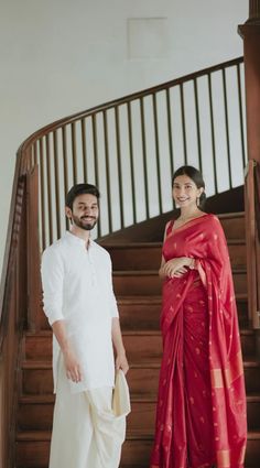 a man and woman standing next to each other in front of a stair case with wooden handrails