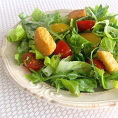 a salad with croutons and lettuce on a white plate sitting on a table