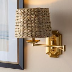 a wall light with a woven shade on it's side next to a framed photograph