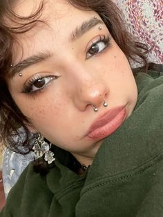 a close up of a person with piercings on her nose and eyes, wearing a green hoodie