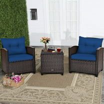 two chairs and a table on a rug in front of a wall with green plants