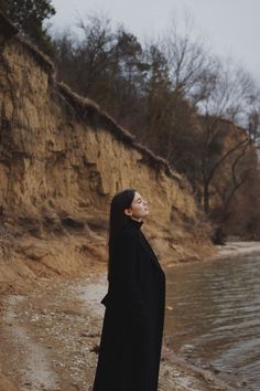 a woman standing on top of a sandy beach next to the ocean with her eyes closed