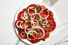 a white plate topped with sliced tomatoes and onions on top of a marble countertop