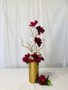 a gold vase filled with red flowers on top of a white cloth covered tablecloth