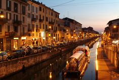 a boat traveling down a river next to tall buildings at night with street lights on