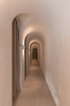 a long narrow hallway with white walls and light at the end is lit by lights on either side