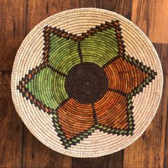 a woven basket with an orange and green flower design on the bottom, sitting on a wooden floor