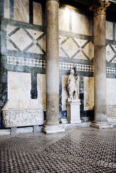 an old building with columns and statues on the floor, in front of it is a mosaic tiled wall