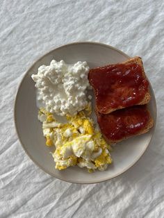 a plate with eggs, toast and jam on it sitting on a white table cloth