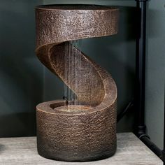 a metal water fountain sitting on top of a wooden table next to a black wall