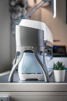 a white blender sitting on top of a counter next to a potted plant