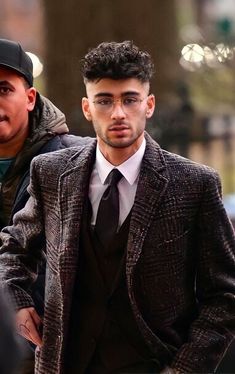 a man in a suit and tie walking down the street with another man behind him