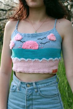 a woman wearing a blue and pink knitted crop top with flowers on the chest