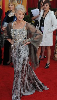 an older woman in a silver dress on the red carpet with other people behind her