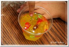 a plastic cup filled with gummy bears on top of a wooden table next to a person's hand