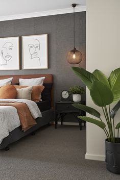 a bedroom with a bed, plant and two pictures on the wall above it's headboard