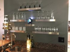 a kitchen counter with wine glasses and bottles on the shelves above it, next to a sink