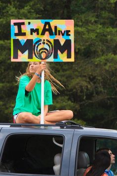 a woman sitting on top of a car holding a sign that says i'm alive mom